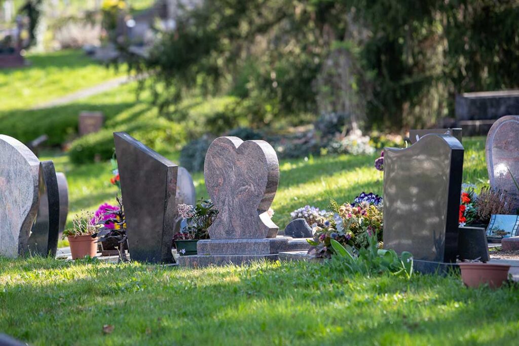 A close view of granite, marble, and bronze headstones standing in a green cemetery after rainfall.