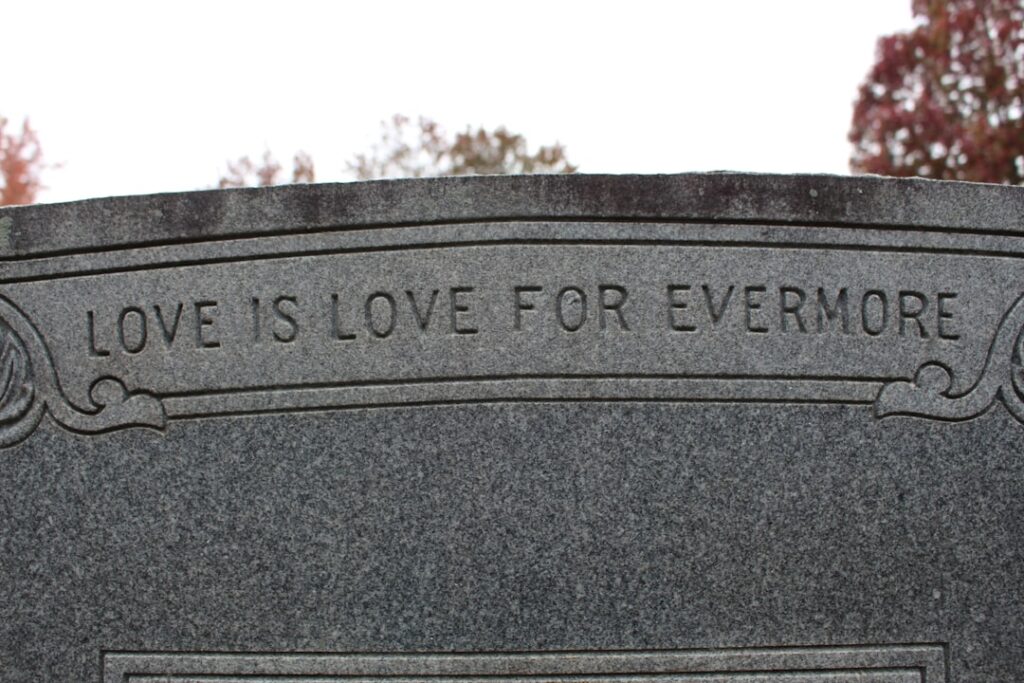 A close-up of a gravestone with engraved artwork, personalized epitaph, and a small ceramic photo inset.