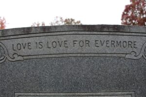 A close-up of a gravestone with engraved artwork, personalized epitaph, and a small ceramic photo inset.